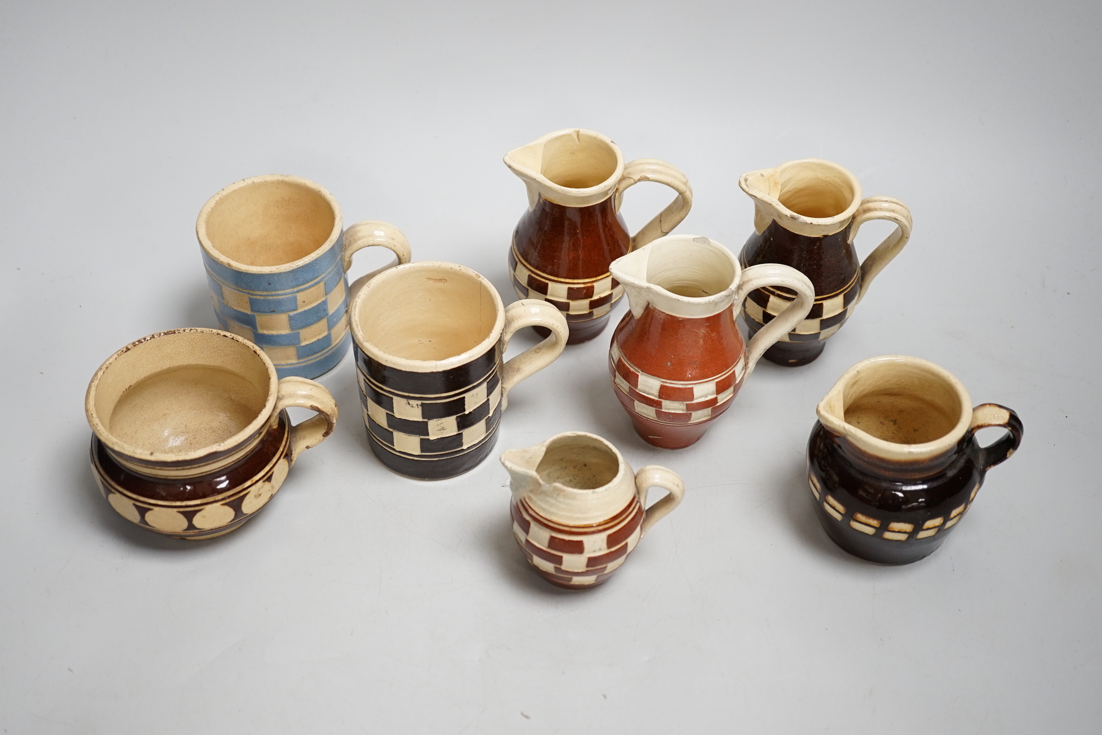 Eight 19th century slip-decorated creamware chequer-pattern jugs and mugs, tallest 10cm
